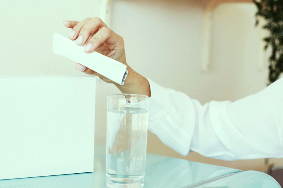 person pouring powder from stick package into glass of water